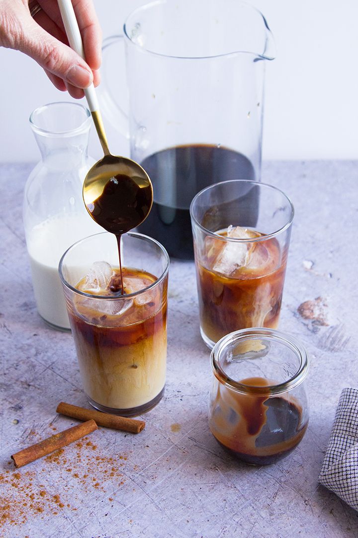 someone is pouring something into some glasses with cinnamon sticks on the table next to them