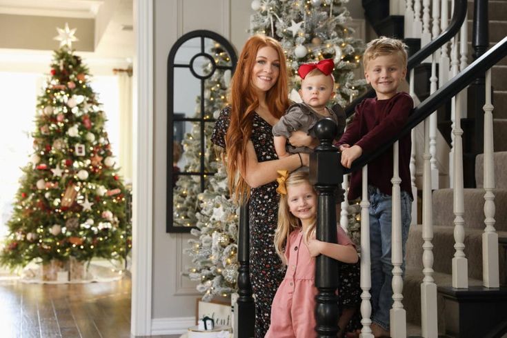 a woman and two children are standing in front of a christmas tree on the stairs