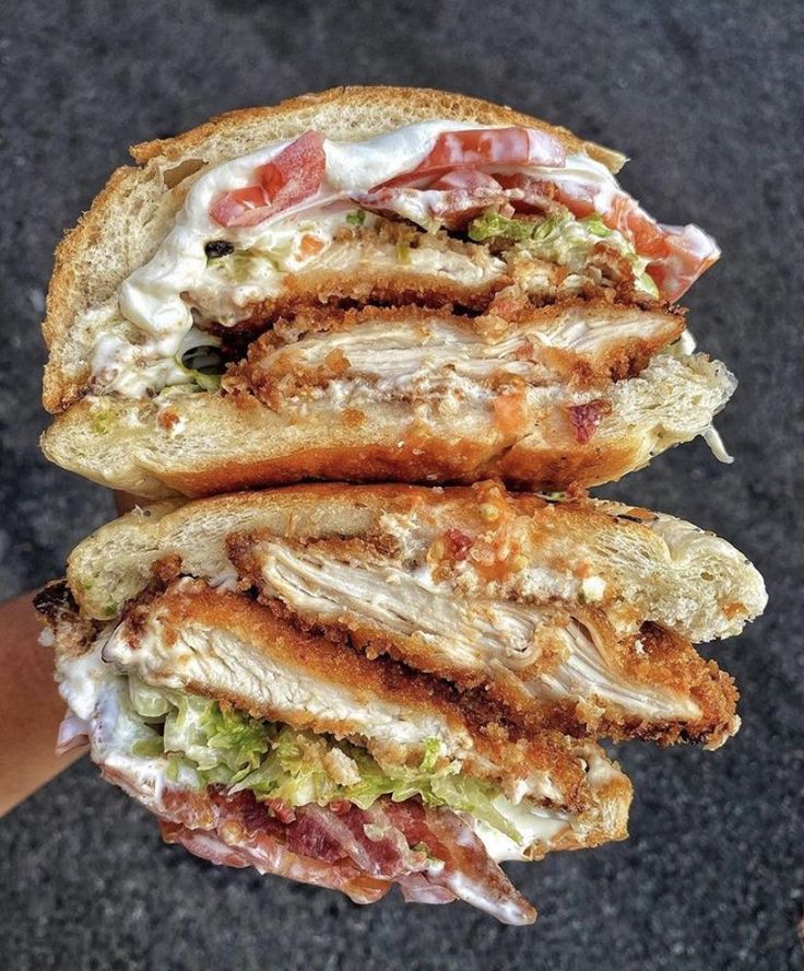 two halves of a sandwich with meat, cheese and lettuce on it being held by a person