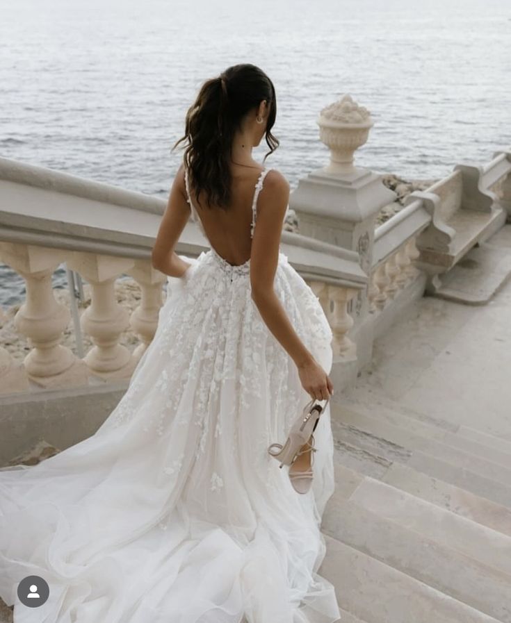 a woman in a white dress is walking down some stairs by the water and looking at something