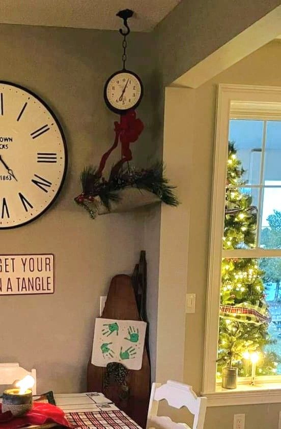 a clock on the wall above a table with chairs and a christmas tree in front of it