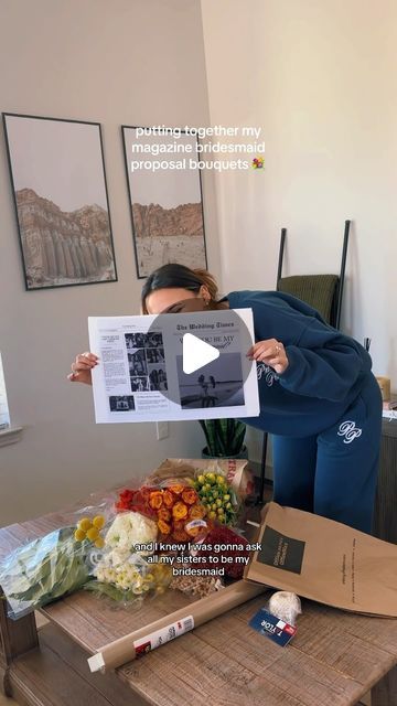 a woman holding up a piece of paper in front of her face while standing next to a table