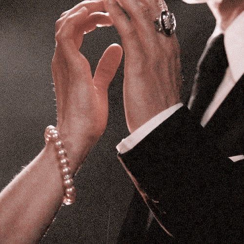 two people are holding hands together and one has a ring on his left hand while the other is wearing a suit