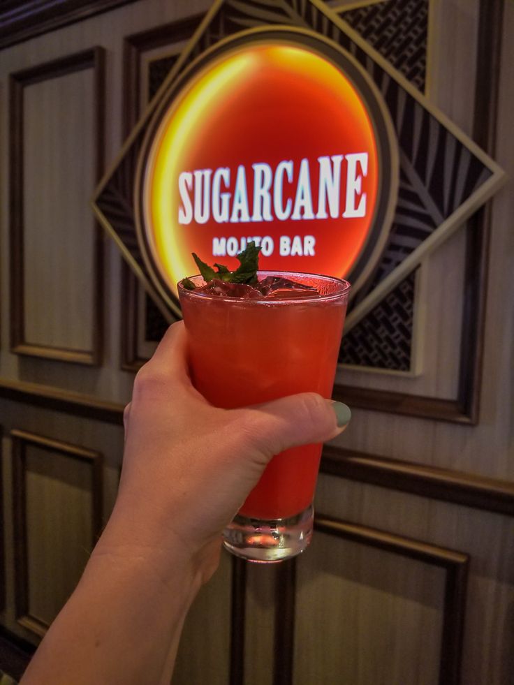 a person holding up a drink in front of a sign that says sugar cane moto bar