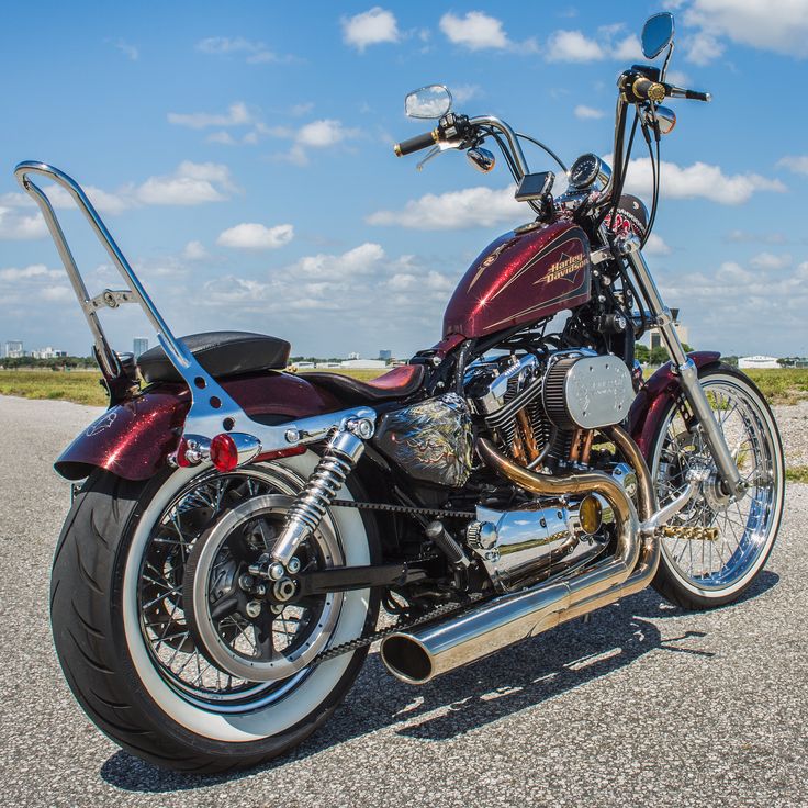 a red motorcycle is parked on the side of the road in front of some clouds