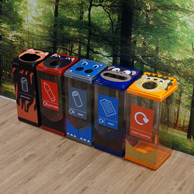 four colorful trash cans sitting on top of a wooden floor next to a forest wall