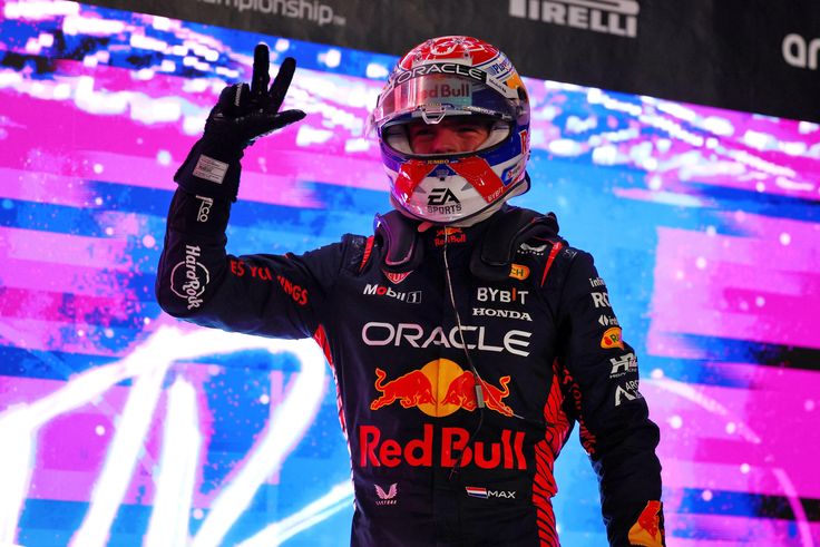 a red bull driver waves to the crowd in front of a large screen with his hand up