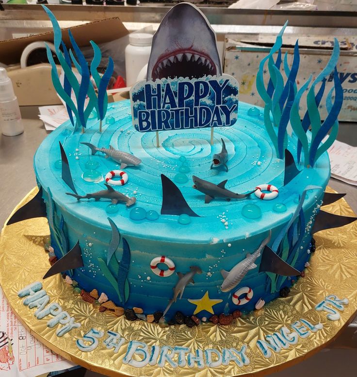 a birthday cake decorated with blue frosting and shark decorations on top of a gold plate