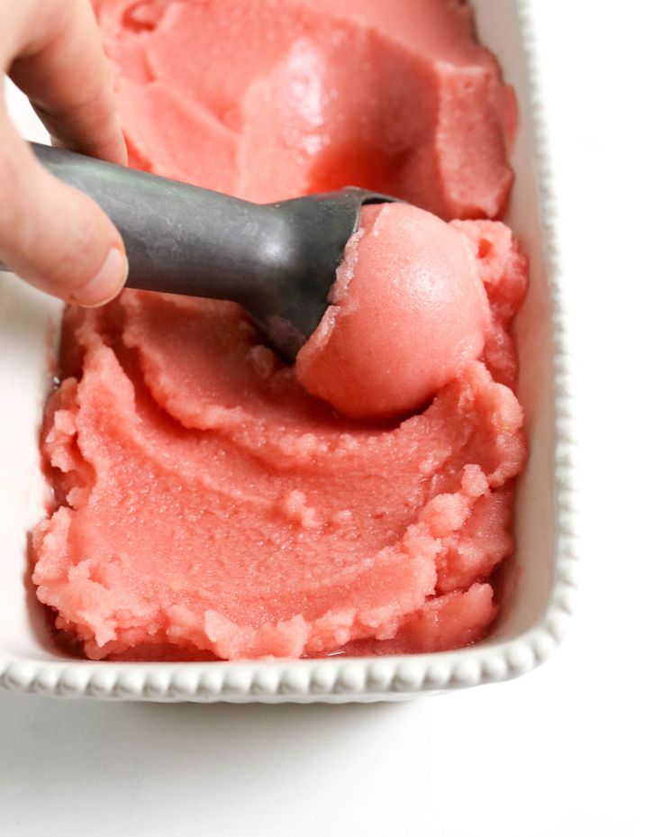 someone is using a spoon to scoop ice cream into a white bowl with pink icing