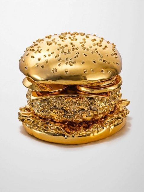 a gold burger with lots of golden toppings sitting on top of eachother