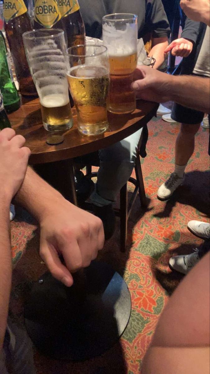 several people are sitting at a table with beers in front of them and one person is holding a beer mug