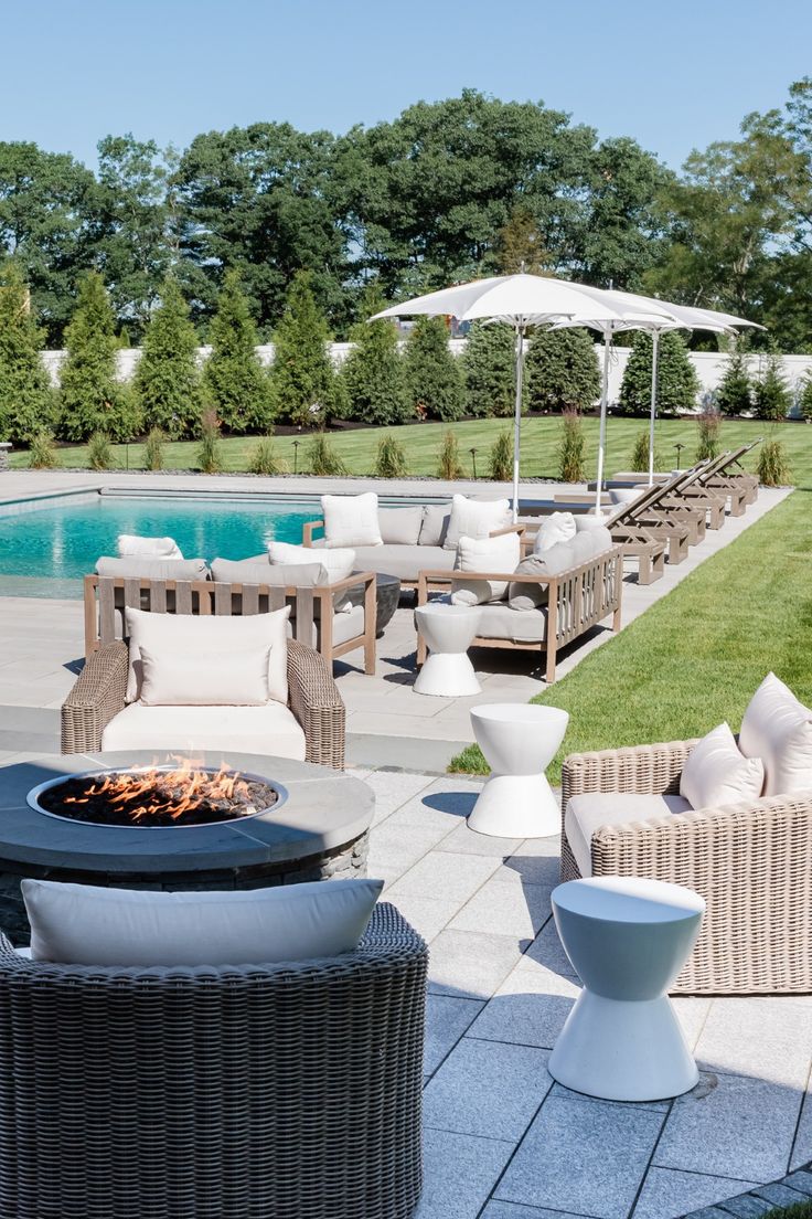 an outdoor patio with chairs and tables next to a fire pit in front of a swimming pool