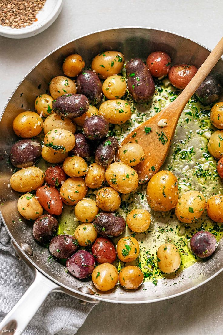 a pan filled with potatoes and other vegetables on top of a white table cloth next to a wooden spoon