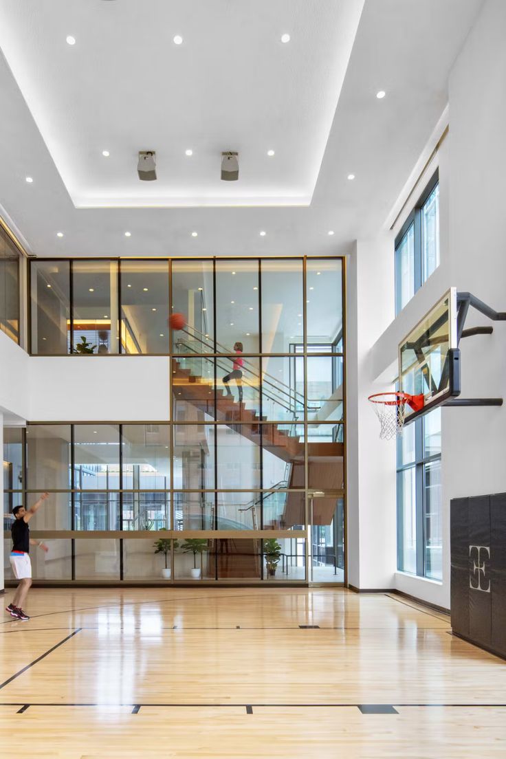 an empty gym with basketball hoop and stairs in the center, surrounded by large windows