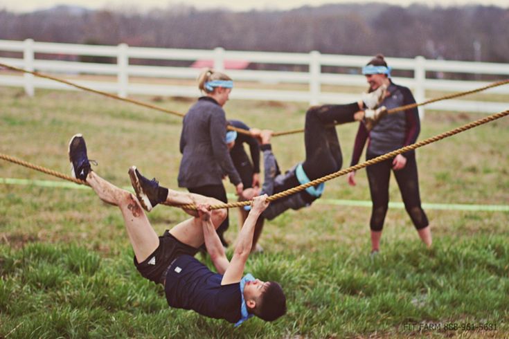 three people are hanging on ropes in a field while one man is doing a handstand