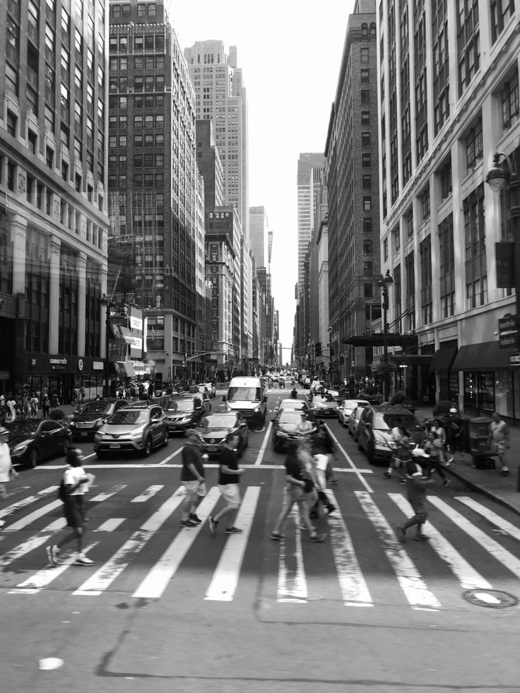 black and white photograph of people crossing the street in new york city, ny with buildings on either side