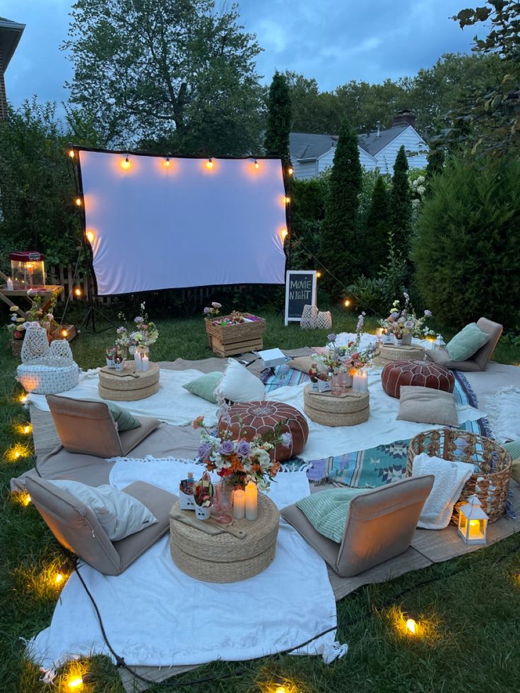 an outdoor movie is set up in the backyard with lights around it and pillows on the ground