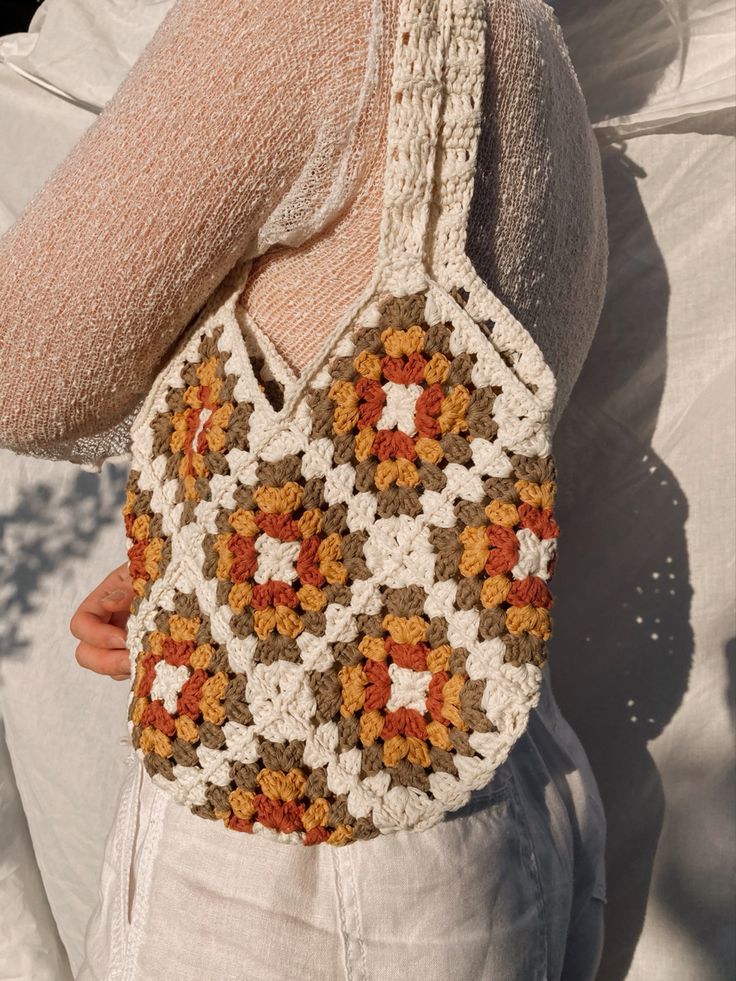 a woman is holding a crocheted bag in her right hand and wearing white pants