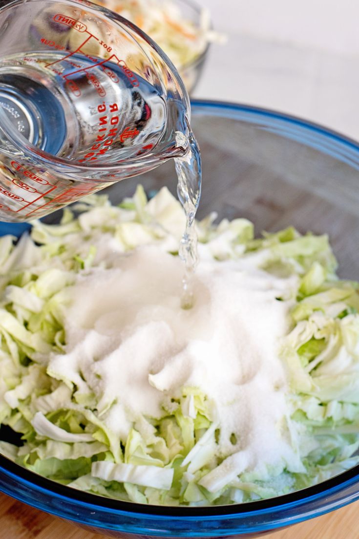 a bowl filled with shredded lettuce next to a measuring cup full of dressing