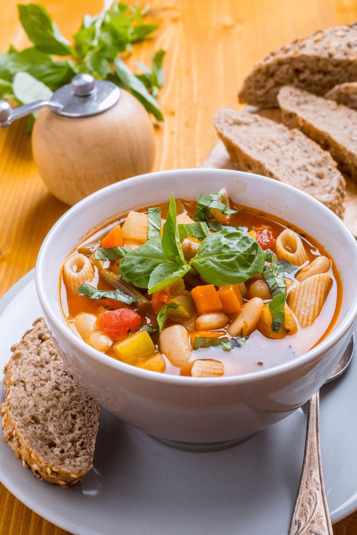 a white bowl filled with pasta and vegetables on top of a plate next to bread