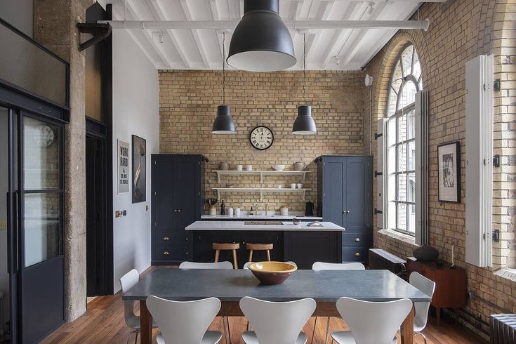 an open kitchen and dining room with brick walls, wood flooring and white chairs