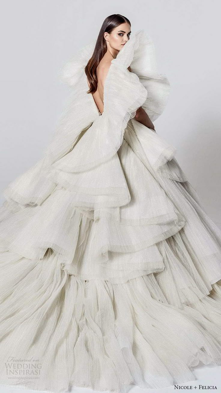 a woman in a white gown with long sleeves and ruffled skirt, posing for the camera