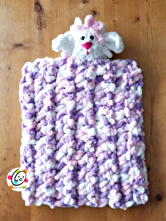 a crocheted blanket with a white and purple animal on it's back