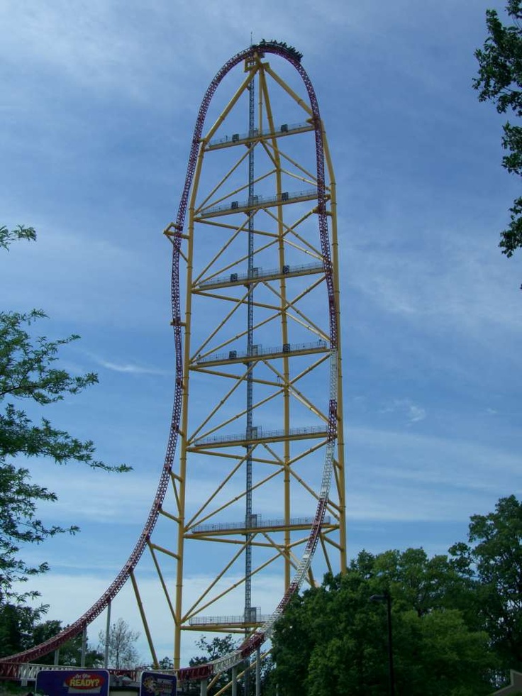 an amusement park roller coaster in the middle of trees and blue sky with white clouds