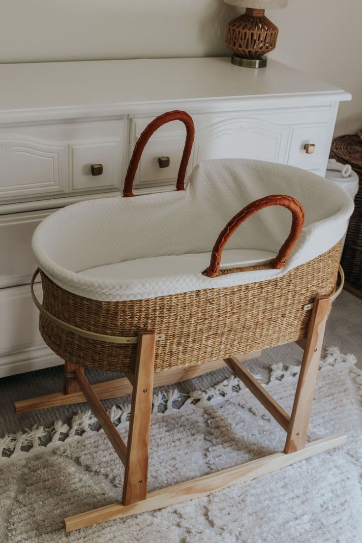 a baby's bassinet with two handles on top of it in front of a dresser