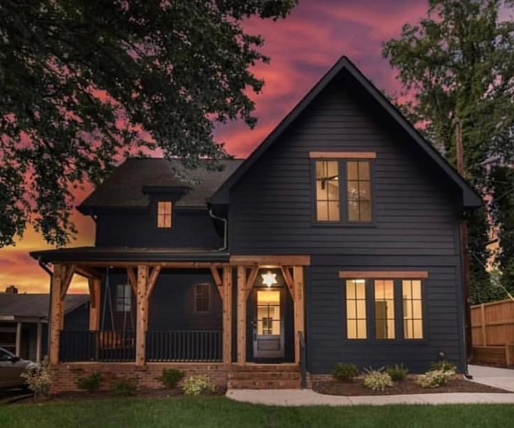 a black house is lit up at night with the sun going down in the background