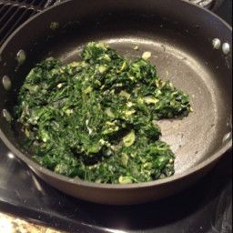 spinach is cooking in a skillet on the stove with other food items nearby