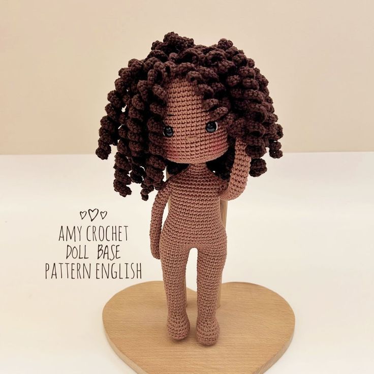 a crochet doll with curly hair standing on a wooden stand and looking at the camera