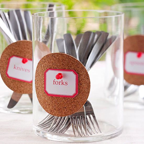 there are forks and spoons in glass cups on the table with name tags attached to them