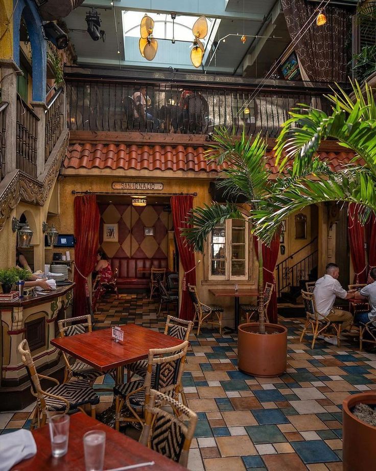 the inside of a restaurant with tables, chairs and potted plants on the floor