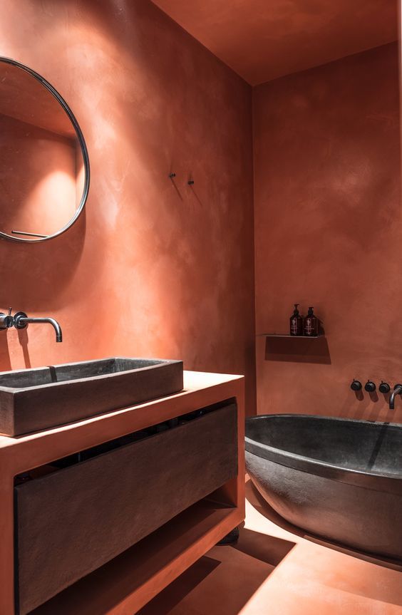 a bathtub and sink in a bathroom with pink walls, brown flooring and an oval mirror on the wall