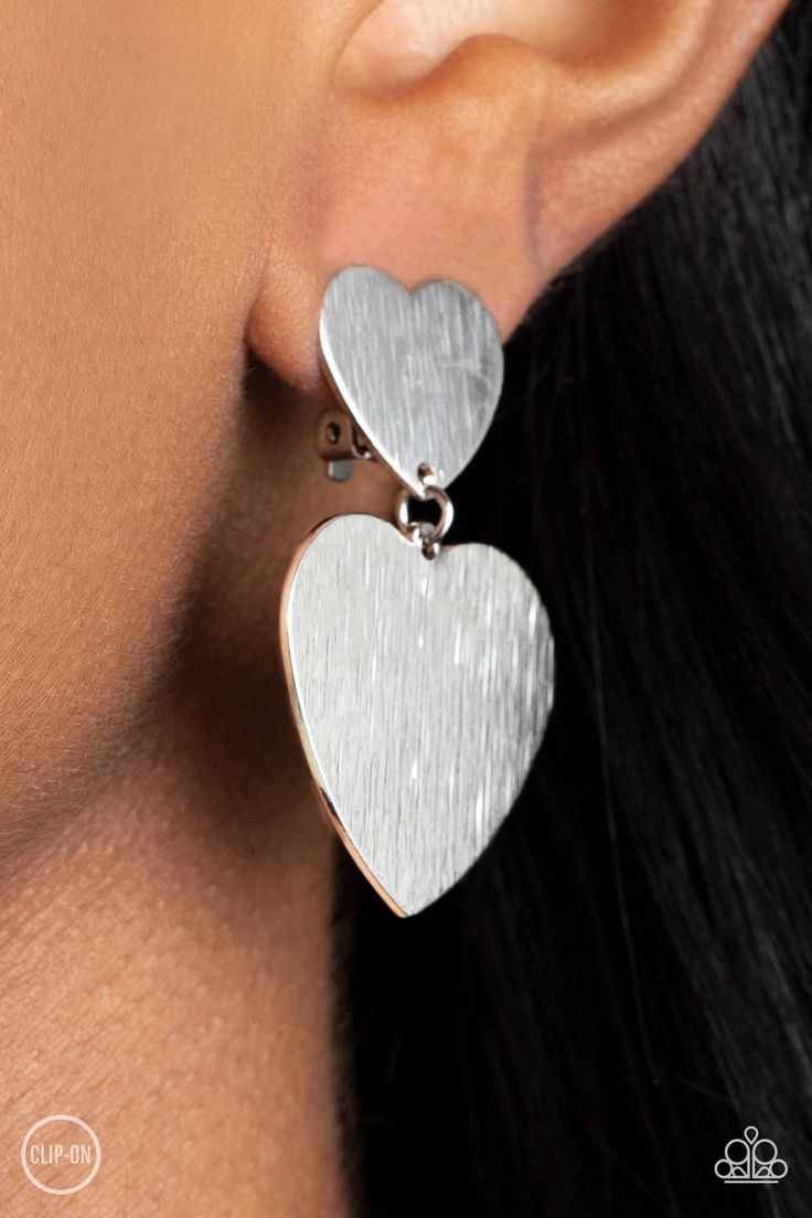 Featuring a shimmery scratched finish, an oversized silver heart charm swings from the bottom of a smaller silver heart charm, resulting in a flirtatious lure. Earring attaches to a standard clip-on fitting.

Sold as one pair of clip-on earrings. Coil Bracelet, Paparazzi Accessories, Rhinestone Bracelet, Paparazzi Jewelry, White Earrings, Boutique Jewelry, Silver Heart, Pearl Bracelet, Heart Charm