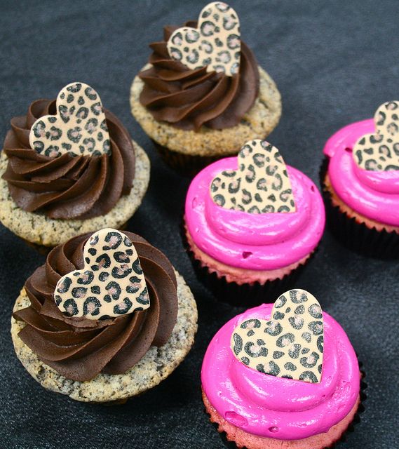 cupcakes decorated with chocolate frosting and leopard print heart decorations on black surface