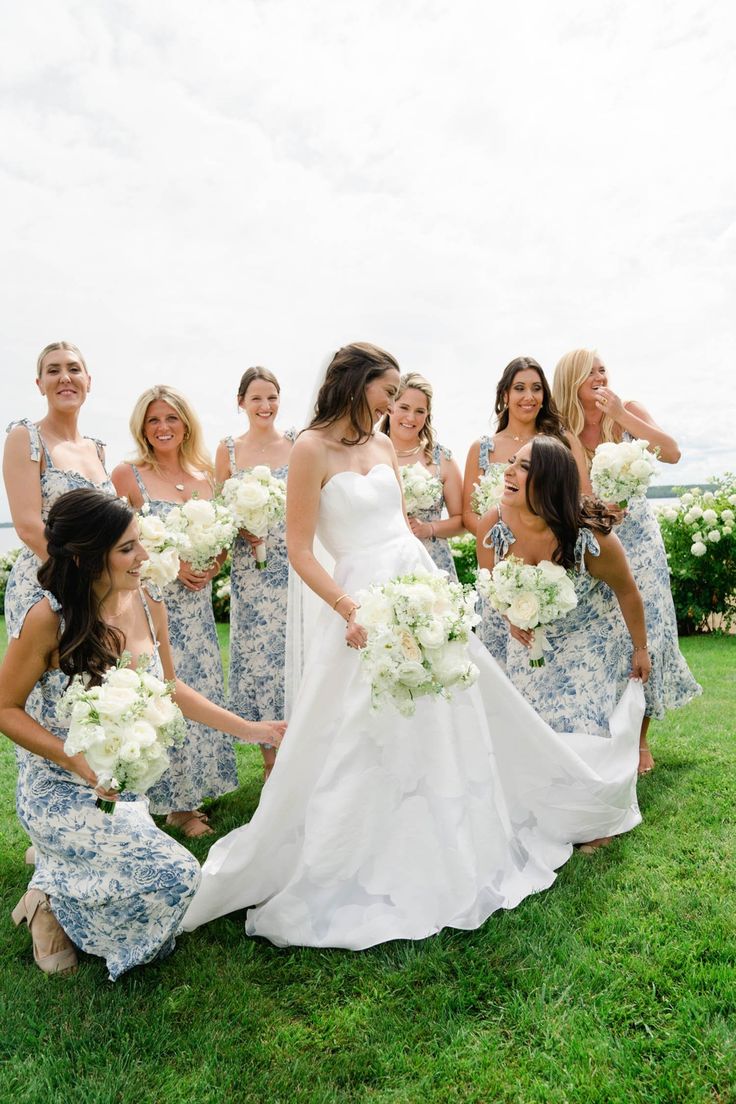 a group of women standing around each other on top of a lush green field holding bouquets