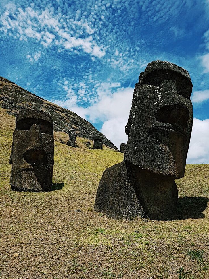 two large statues sitting on top of a grass covered hill under a blue sky with wispy clouds