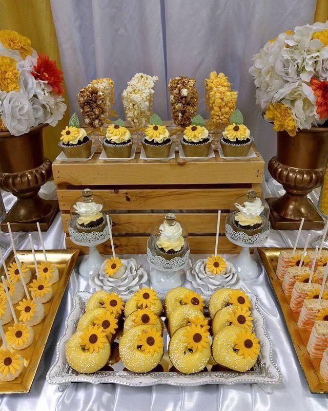 sunflower cupcakes are displayed on a table with other desserts and treats