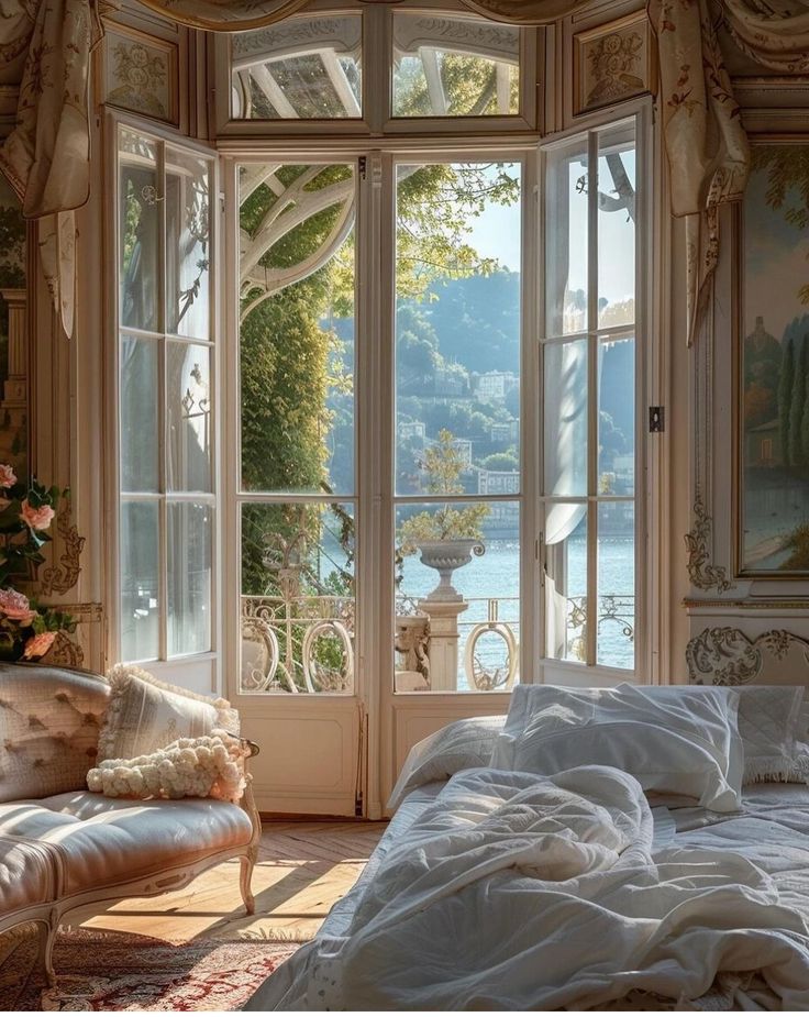 there is a bed with white sheets and pillows in front of an open window that looks out onto the water