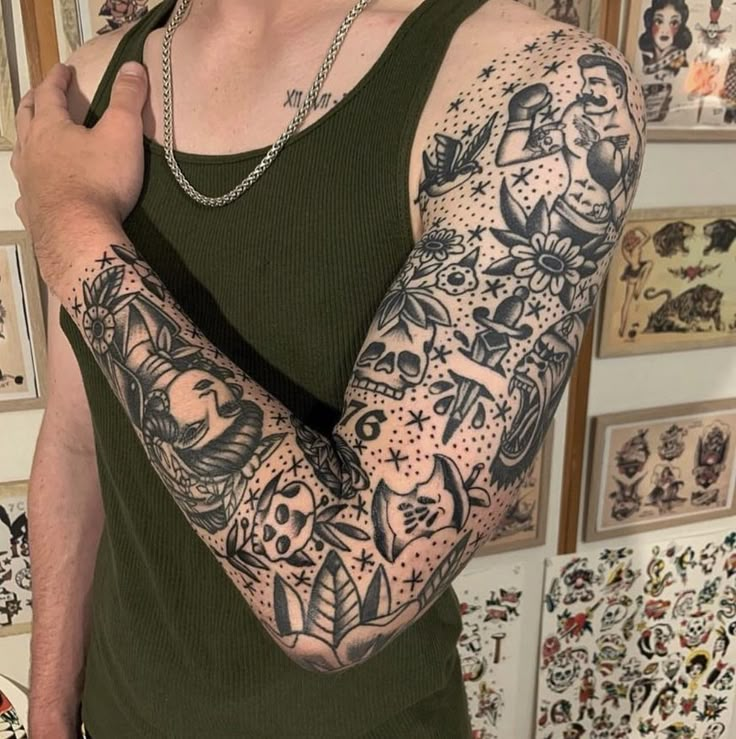 a man wearing a green tank top with tattoos on his arms and shoulder, standing in front of a wall full of pictures