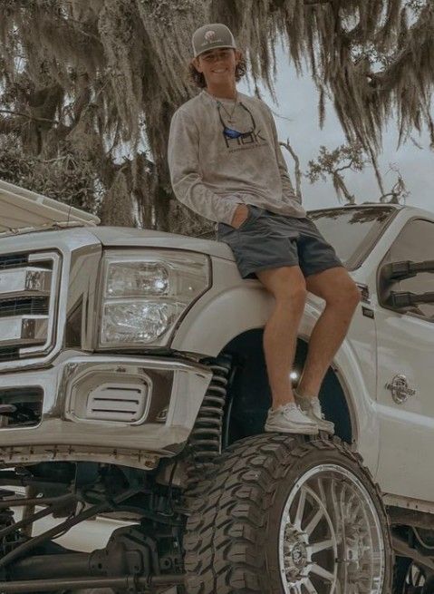 a man sitting on the hood of a white truck with huge tires and rims