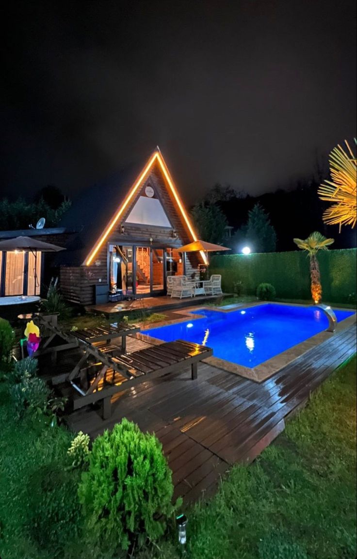 a house with a swimming pool in the yard at night, surrounded by greenery