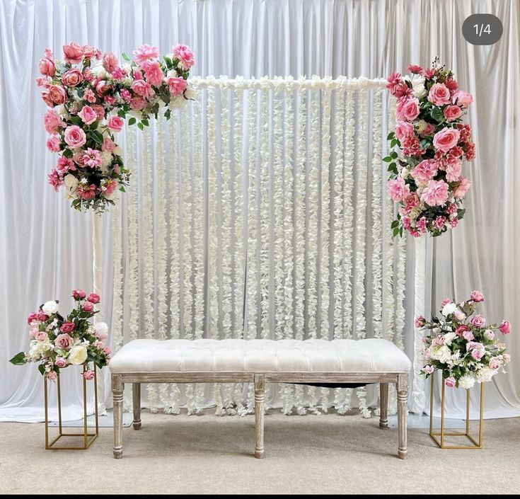 a white bench with flowers on it in front of a curtained wall and two chairs