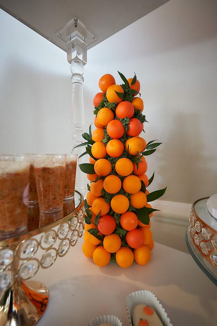 there is an orange tree on the table next to some cups and silver trays