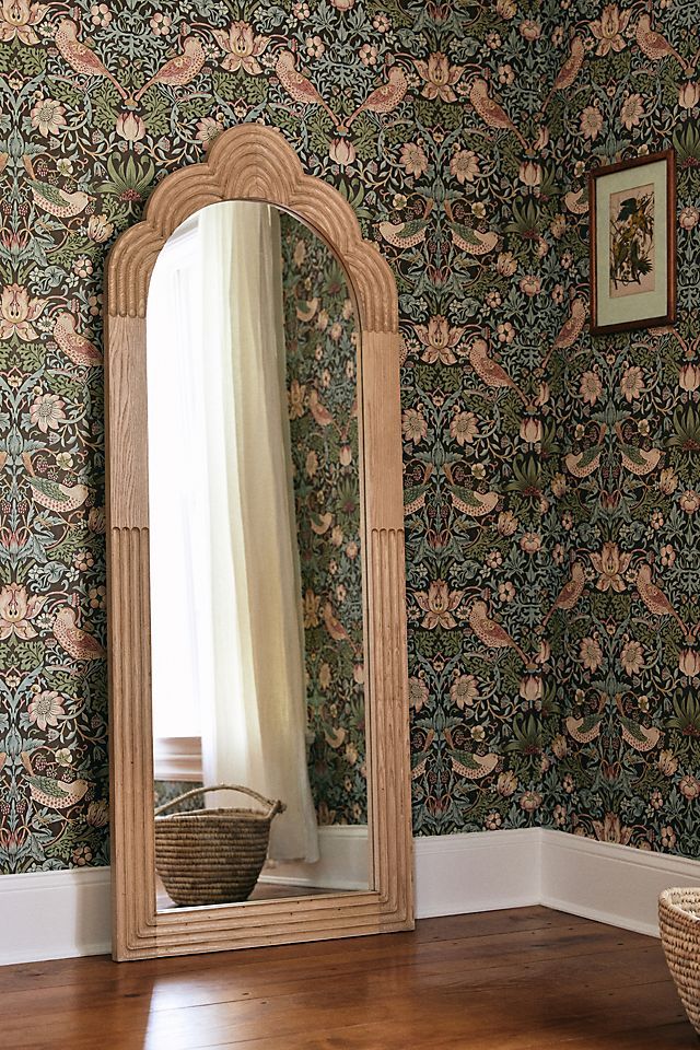 a large mirror sitting on top of a wooden floor next to a wallpapered wall