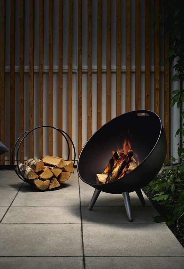 a fire pit sitting on top of a cement floor next to a pile of logs