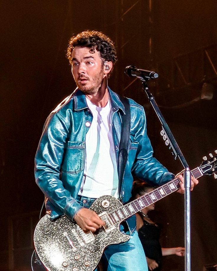 a man with a guitar standing in front of a microphone