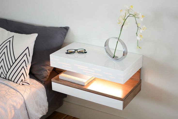 a white table with a flower and some glasses on it, next to a bed